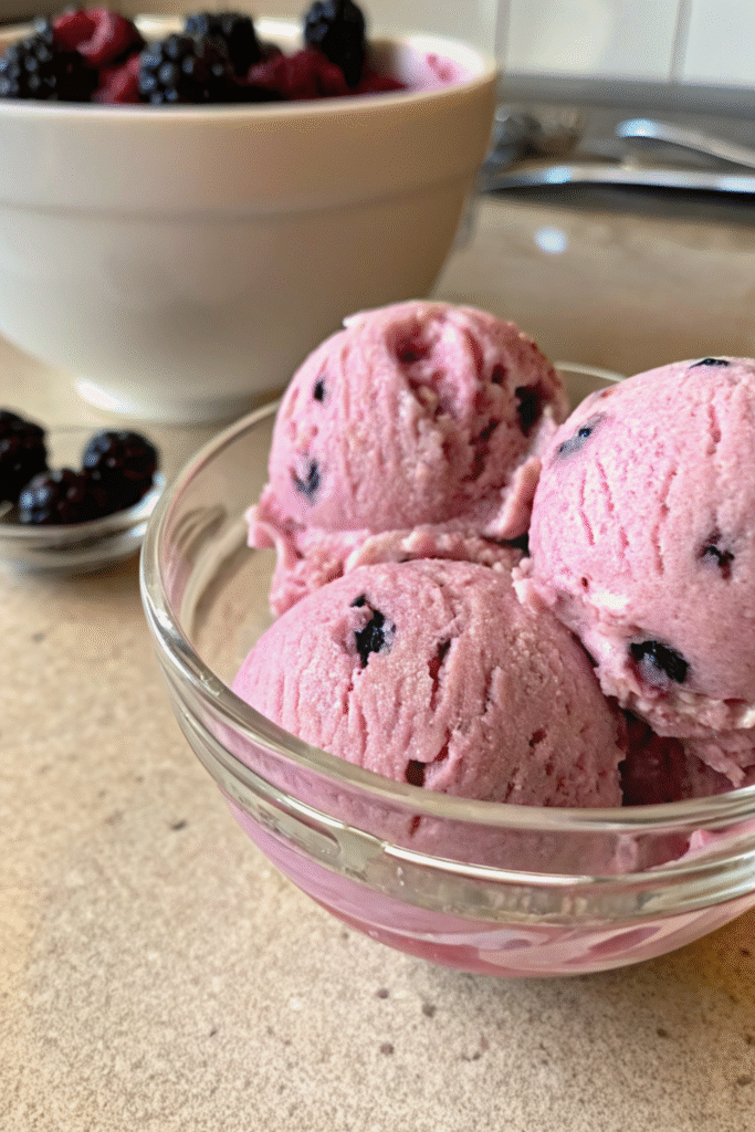 Vegan berry ice cream scoops in a glass bowl.