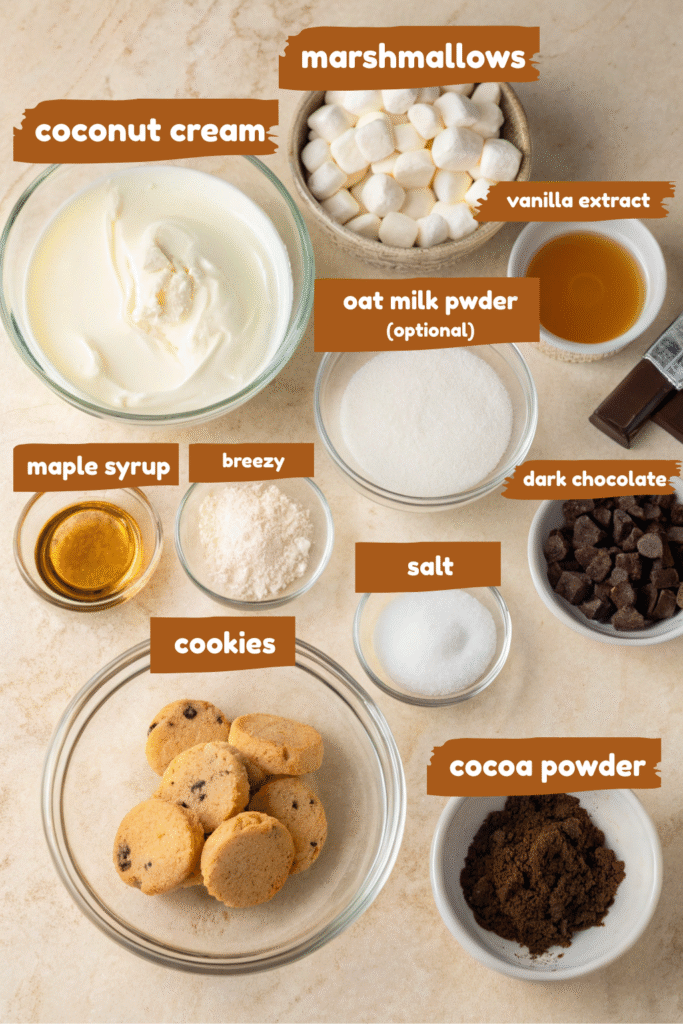 ingredients for dairy-free rocky road ice cream, including marshmallows, cocoa powder, heavy cream, and cookie chunks.