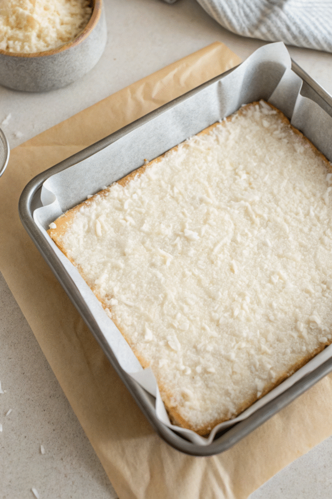 Pressed coconut mixture in a parchment-lined square pan.