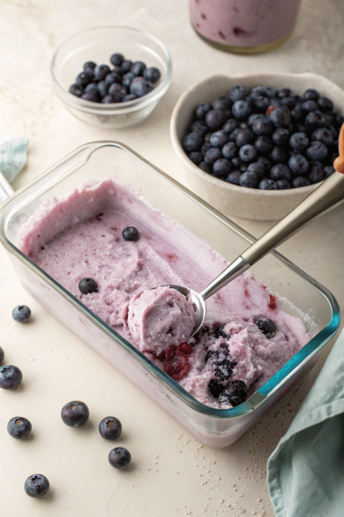 Scooping blueberry vegna ice cream from a glass container.