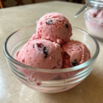 A glass bowl filled with scoops of creamy vegan berry ice cream with berry pieces.