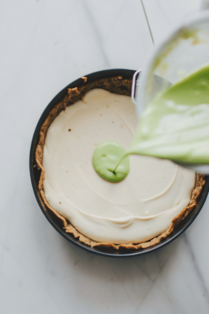 Pouring green matcha filling onto a cheesecake base