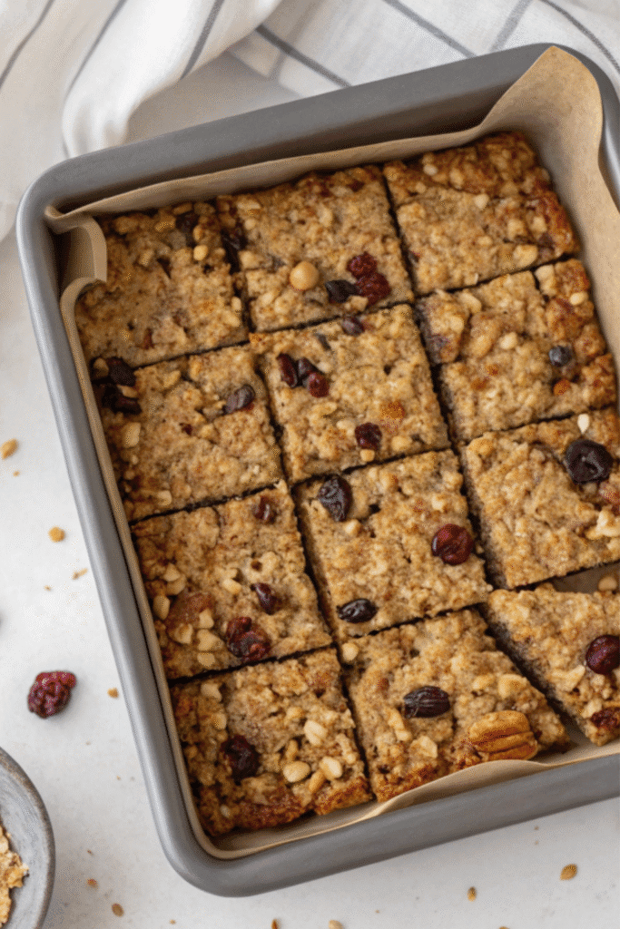 Freshly baked fruit granola bars in a pan, cut evenly into square pieces with cranberries and nuts.