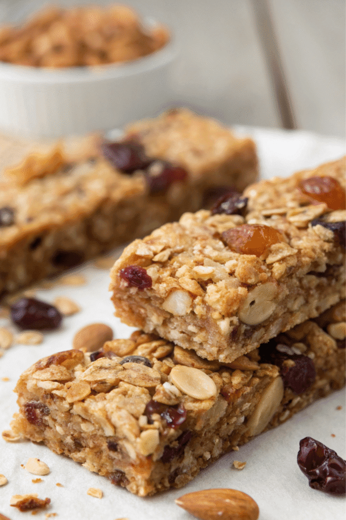 Homemade granola protein bars recipe with oats, nuts, and dried fruit stacked on parchment paper.
