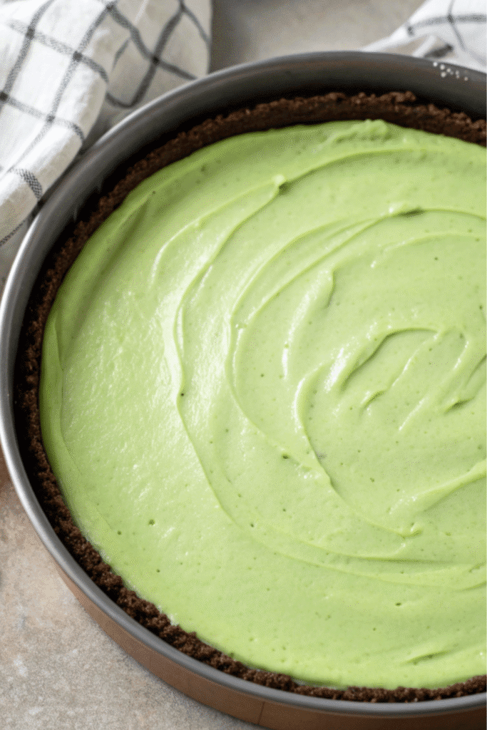 Green Velvet Cheesecake batter evenly spread in a chocolate crust inside a springform pan, ready for baking.