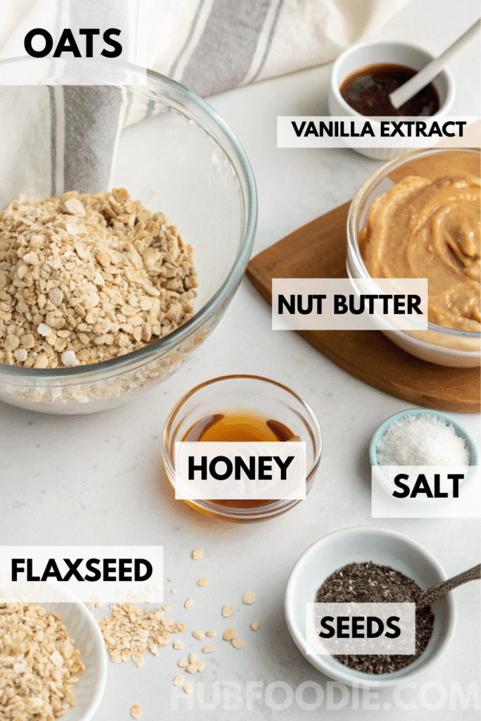Ingredients for homemade gluten free granola bars including oats, nut butter, honey, flaxseed, vanilla extract, salt, and seeds on a white counter.
