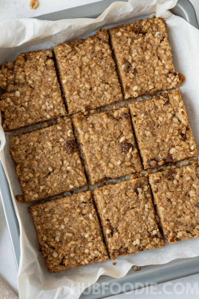 Homemade gluten free granola bars sliced into even squares in a parchment-lined baking pan, ready to store.