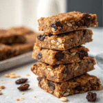 Homemade protein granola bars stacked with oats, nuts, and dried fruit on parchment paper.