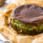 Close-up of a rustic Matcha Basque Cheesecake with a caramelized top and vibrant green center, sitting on crinkled parchment paper.