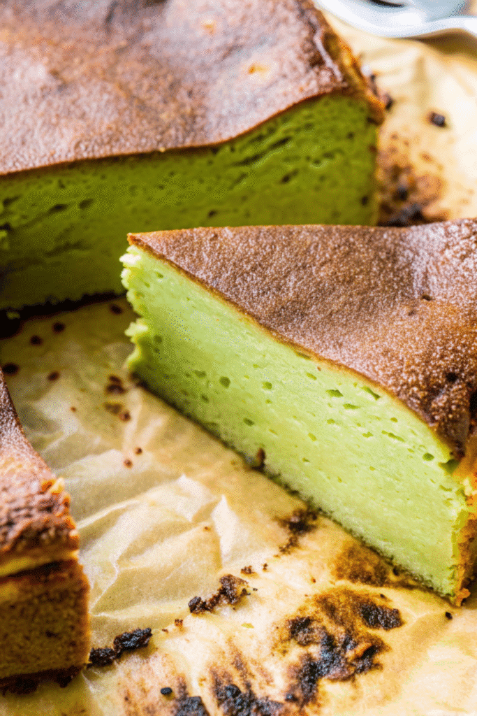 Close-up of a sliced Matcha Basque Burnt Cheesecake with golden-brown crust and vibrant green center on parchment paper.
