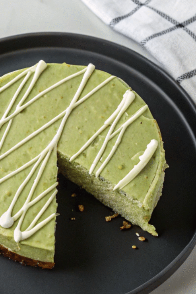 Matcha cheesecake topped with elegant white chocolate drizzle, with a slice removed – Matcha Cheesecake Recipe.