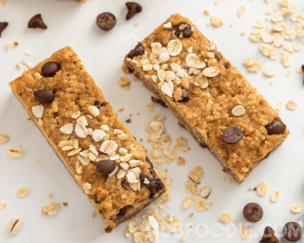 Nut free granola bars baking step in parchment-lined square pan with golden oat mixture and chocolate chips before slicing.