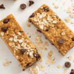 Nut free granola bars baking step in parchment-lined square pan with golden oat mixture and chocolate chips before slicing.