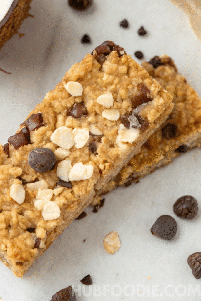 Close-up of nut free granola bars recipe topped with oats, chocolate chips, and seeds on parchment paper.