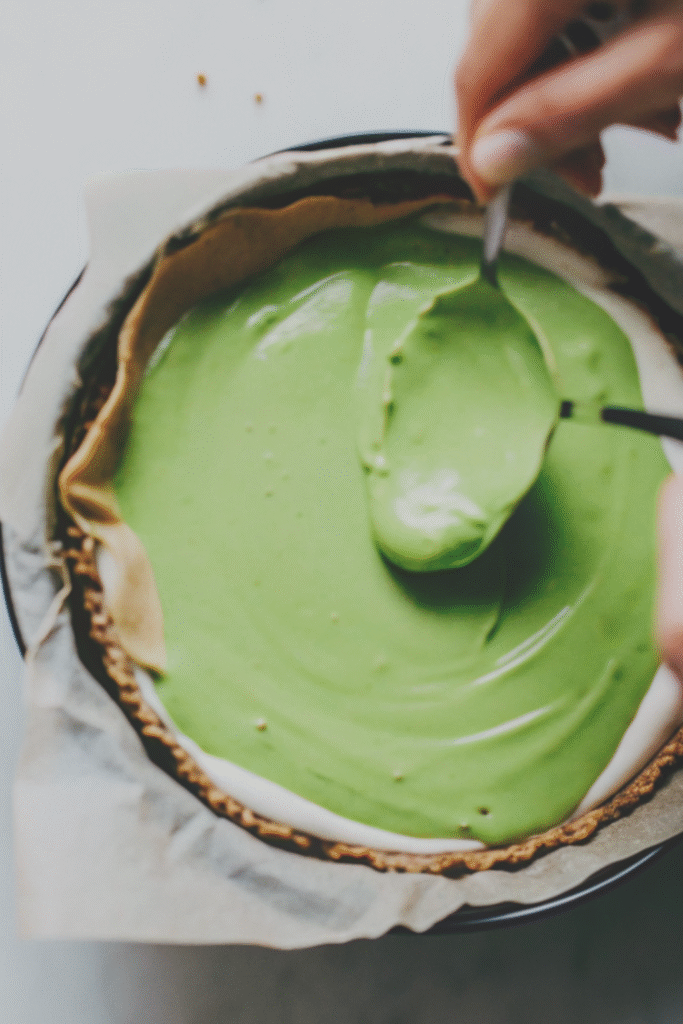 Smoothing the top of a raw matcha cheesecake with a spoon