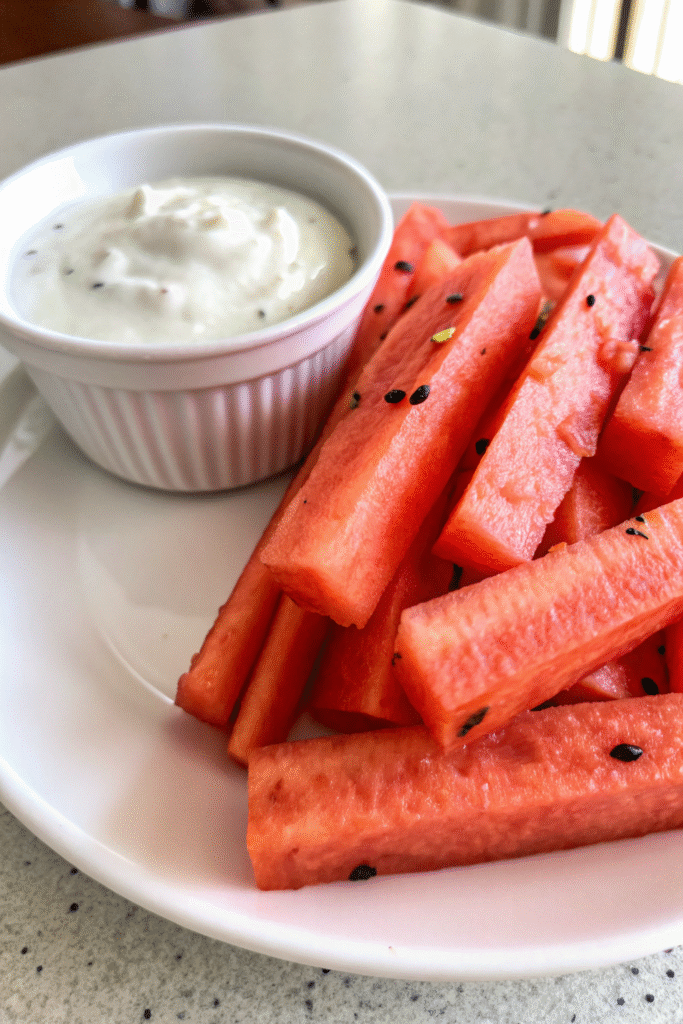 Close-up of watermelon fries served with coconut lime dip in a white ramekin on a plate.