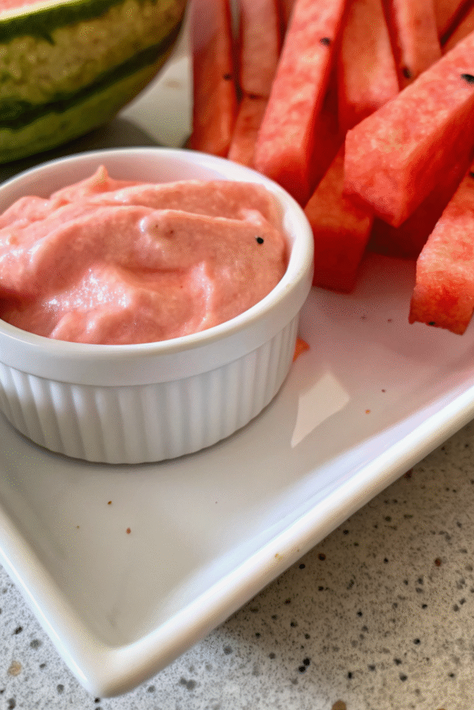 Close-up of watermelon fries with creamy strawberry dip in a white ramekin on a white platter