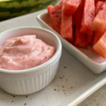 Close-up of fresh watermelon fries served with a creamy strawberry dip in a white ramekin on a beige tray