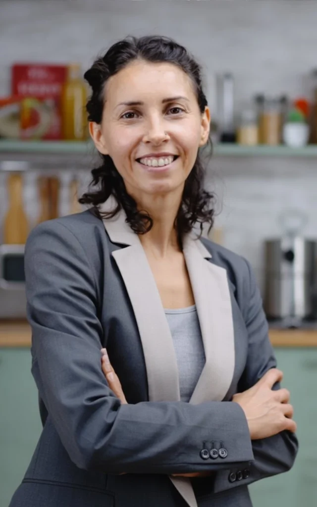Professional woman smiling with arms crossed, standing in a kitchen setting.