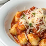 Gnocchi in marinara sauce topped with shredded cheese and garnished with fresh parsley.