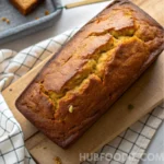 Golden loaf of yellow squash bread resting on a wooden cutting board.